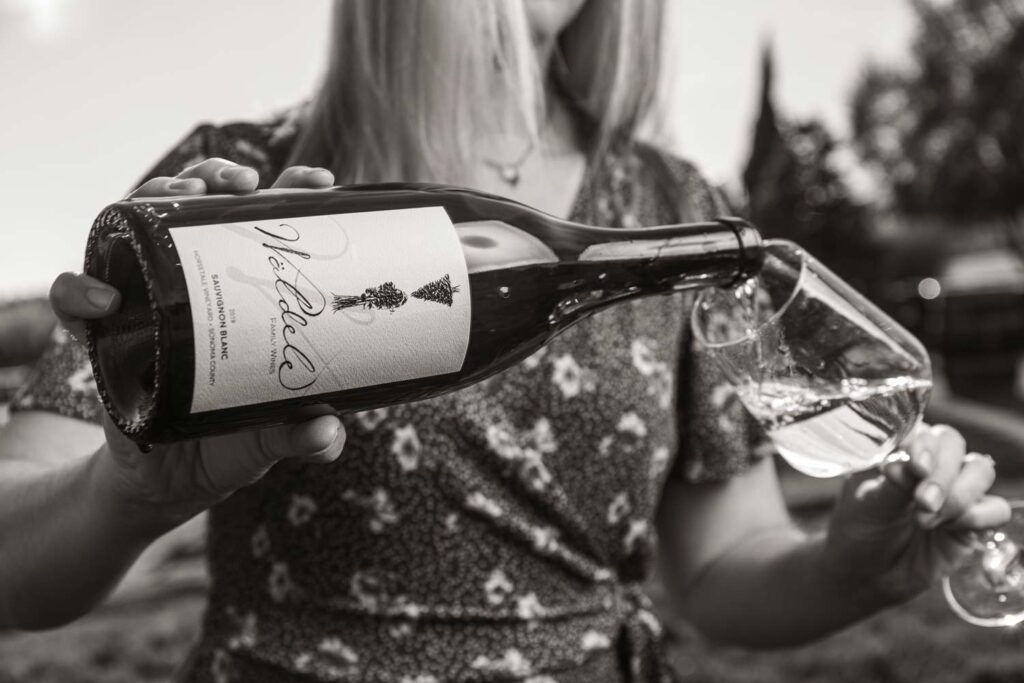 Black and White Image of a woman pouring Waldele family wines, sauvignon blanc into a glass outside